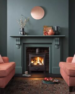 Stunning Victorian fireplace with a dark teal painted surround. Two pink chairs are in front of the hearth.