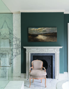 White Georgian style fireplace decorated with swags and drops against a dark teal wall with a landscape painting above the fireplace, A single chair faces the viewer.