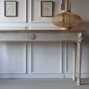 Pale grey painted console table with wood appliques and decorative corbels, set against a matching grey panelled wall.