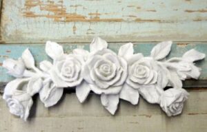 Spray of five white roses as a carved wood applique against a distressed green blue background.