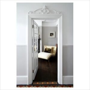 White architrave around a tall door above which is a fret wood carved applique of a shield.
